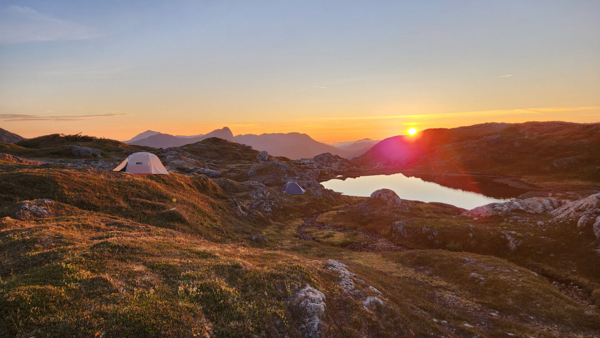 Sunset over mountains with camping tents nearby.