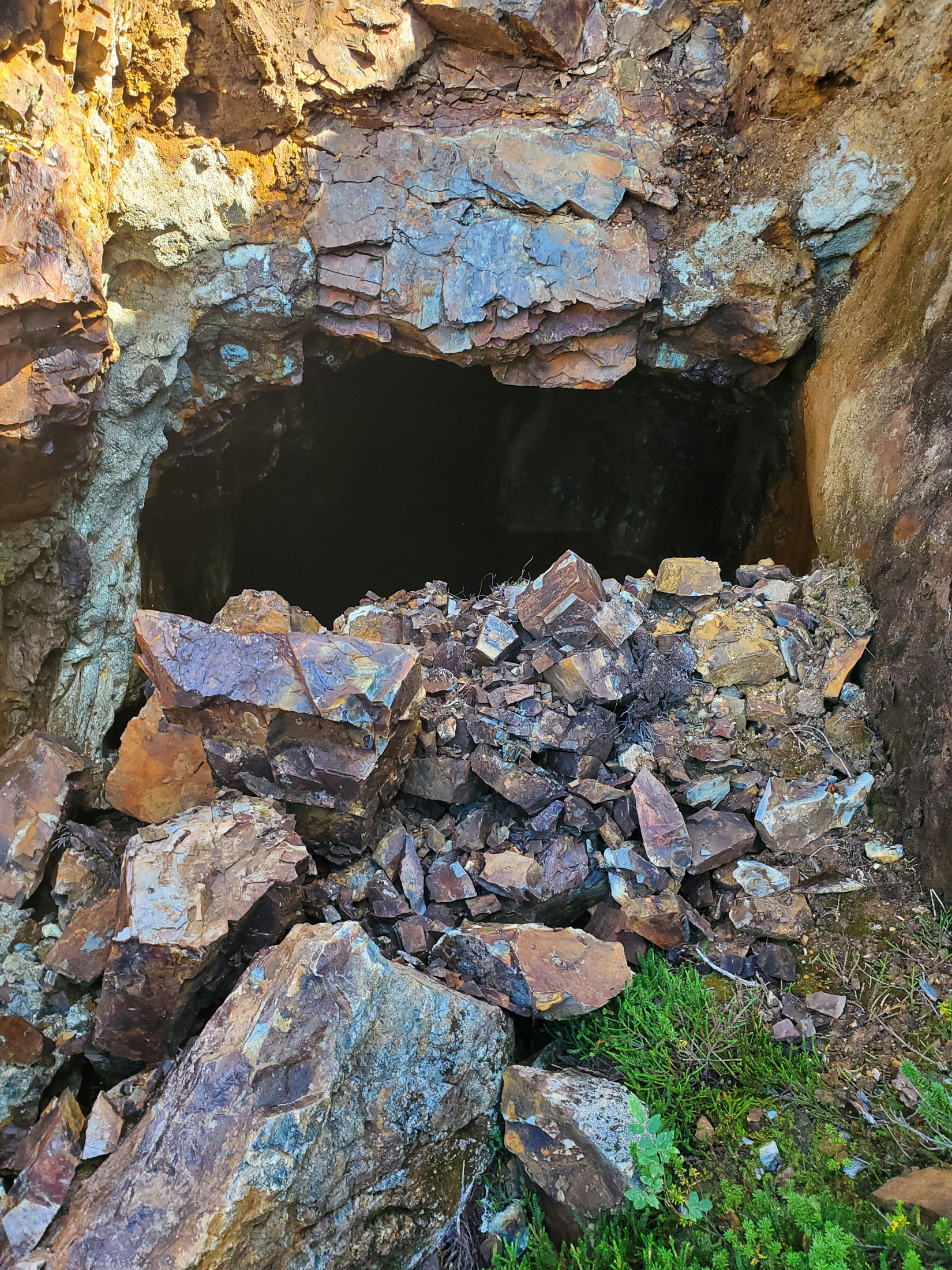Entrance to a rocky cave with scattered stones.